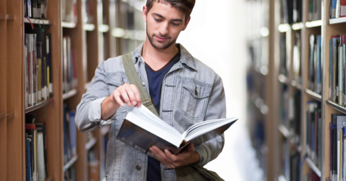 Eine Person steht zwischen zwei Buchregalen und blättert in einem Buch
